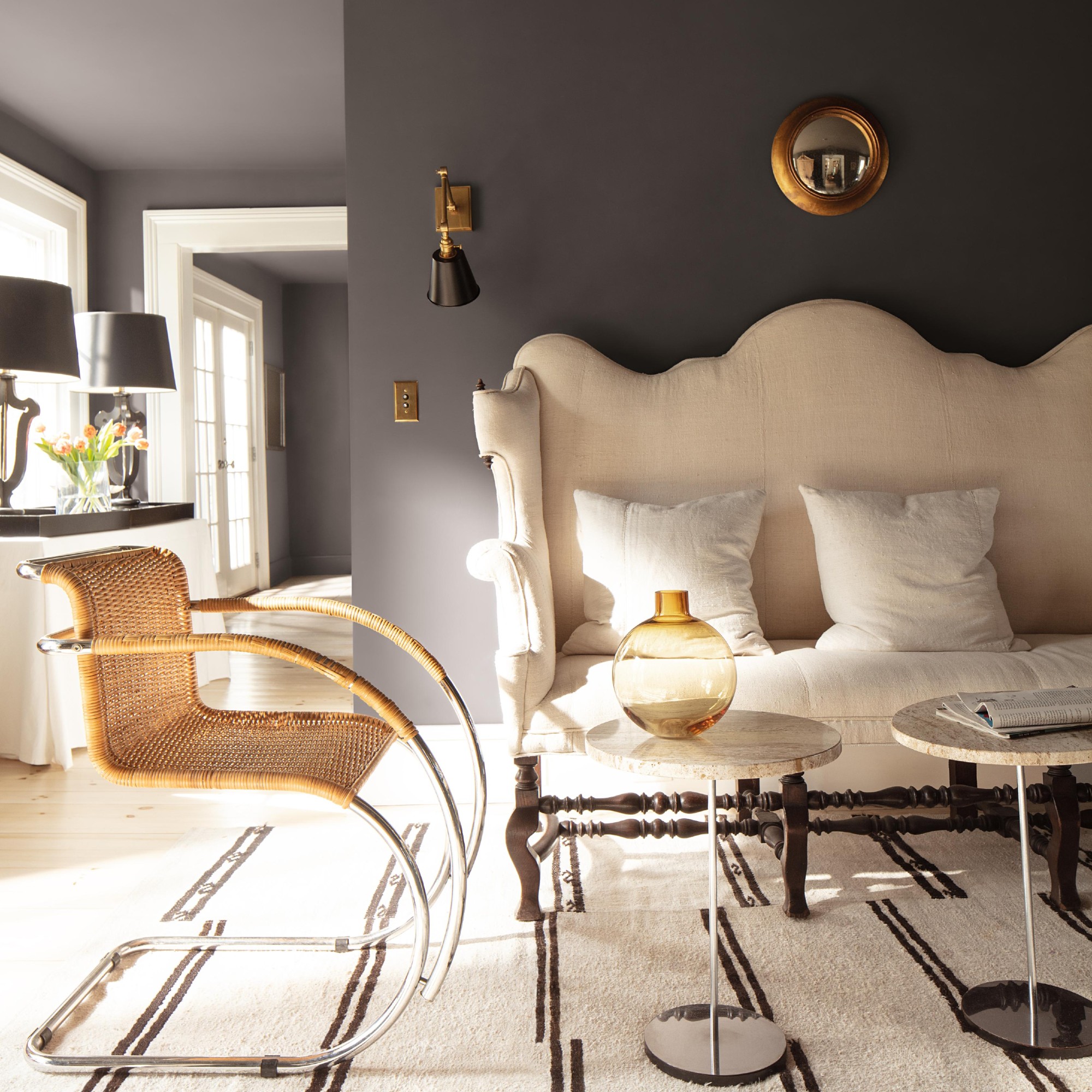 A small living room with a cream sofa and a rattan and chrome chair painted in Benjamin Moore's Silhouette shade, a dark brown with a charcoal undertone
