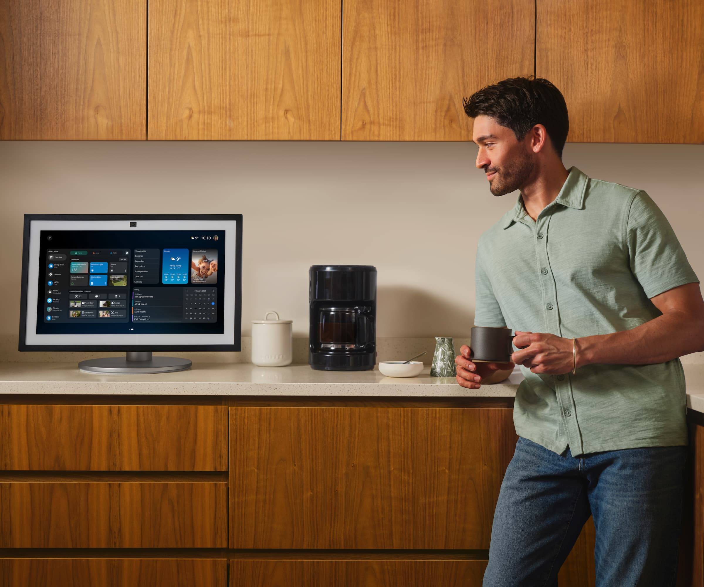 An Alexa smart hub in a kitchen next to a man drinking from a mug