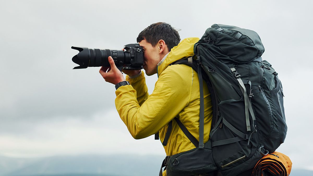 Man with camera on a mountain in a yellow raincoat and backpack with camping gear