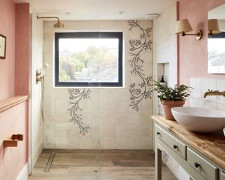 A small bathroom with pink walls and shower wall with floral decorative feature, vanity with sink, and wood floor