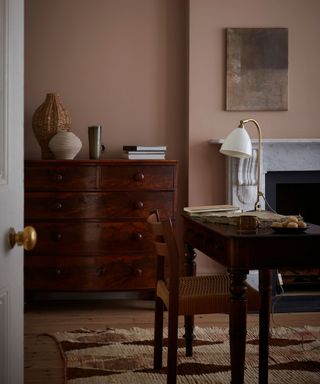 room with light brown walls, vintage wooden dresser, dark wooden table with wooden chair and desk lamp