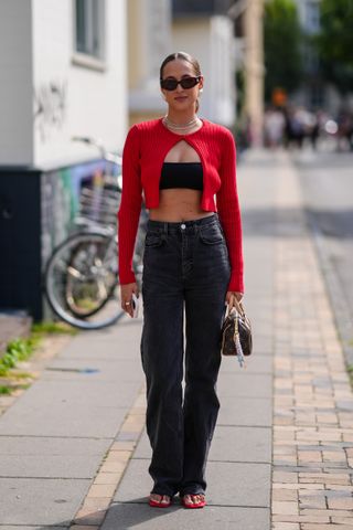 Woman wearing red cardigan, black jeans and red flip-flops with black sunglasses and Louis Vuitton bag during Copenhagen Fashion Week.