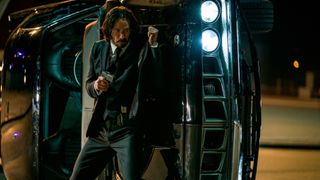 John Wick shelters behind an upturned car in a gun fight