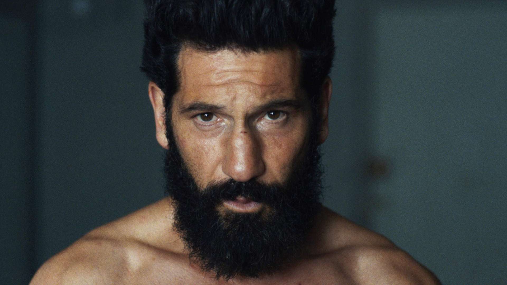 Head and shoulders image of Jon Bernthal's Frank Castle sporting a beard, shirt-less, and looking into the camera in The Punisher: One Last Kill