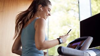 Woman wearing headphones using smartphone while running on treadmill