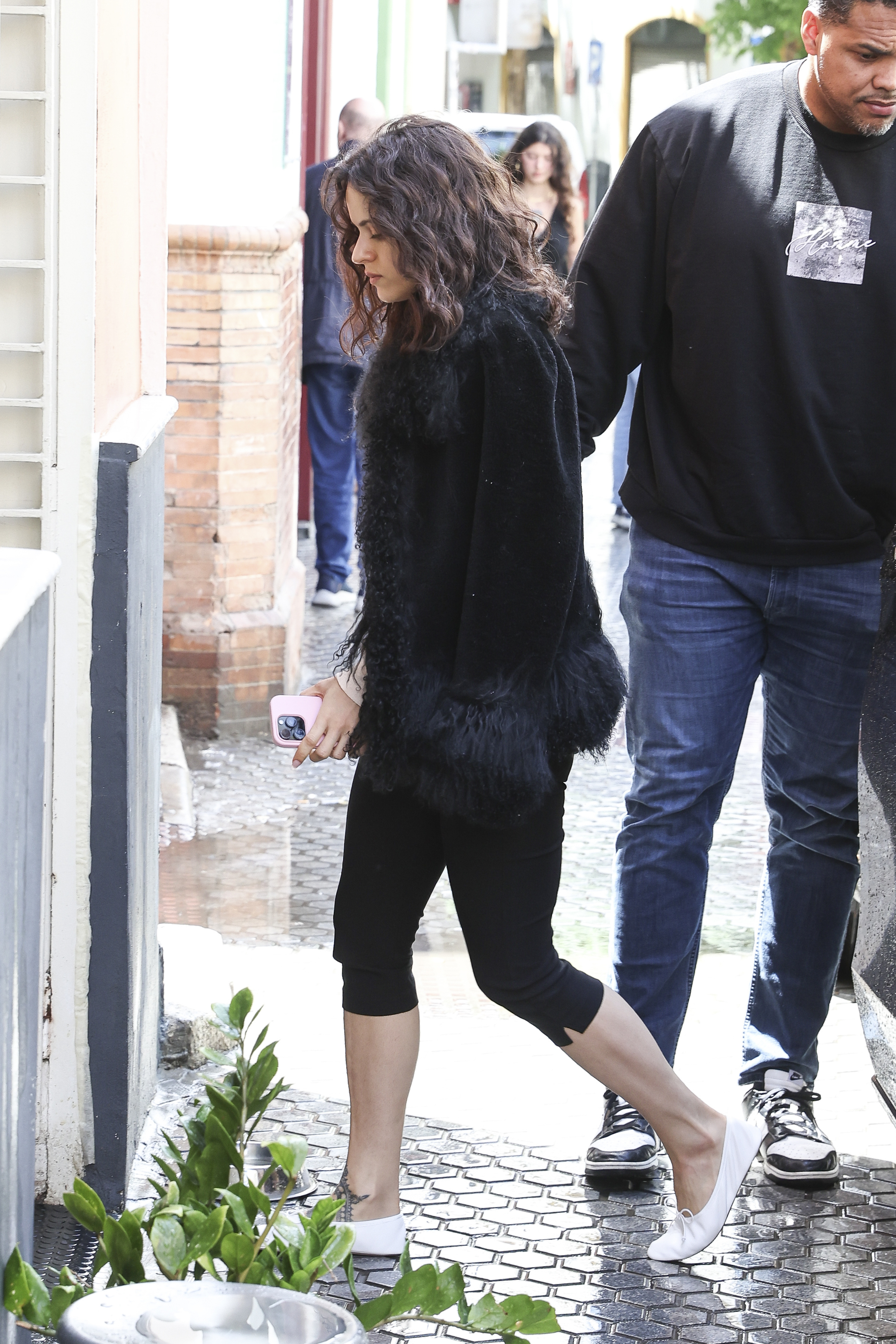 Rosalia in Seville wearing a jacket with a faux-fur trim, black capri pants, and white high-vamp ballet flats