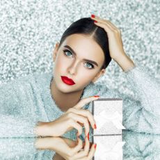 best luxury beauty gifts - woman wearing silver sparkly jumper and a red lip holding onto a present - gettyimages 898813626