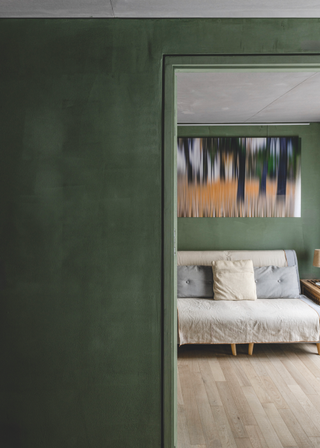 A dark green wall leads on to a small cream sofa, with an abstract painting in orange and black on the wall.