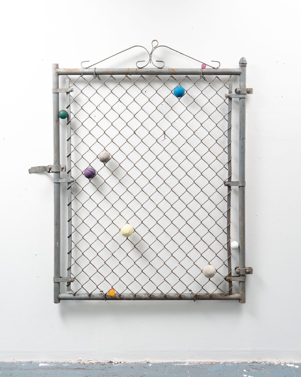 A metallic fence with a floral-inspired decoration at the top features colorful tennis balls stuck in its components.