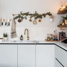 kitchen sink area with white cabinets, gold mixer tap and garland on the wall