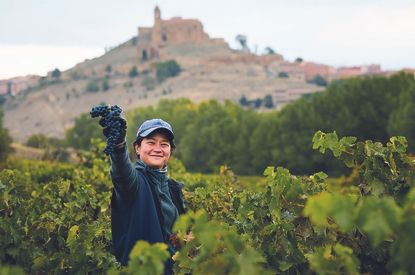 Jade Gross among vines, the castle of San Vicente de la Sonsierra visible in the background