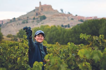 Jade Gross among vines, the castle of San Vicente de la Sonsierra visible in the background