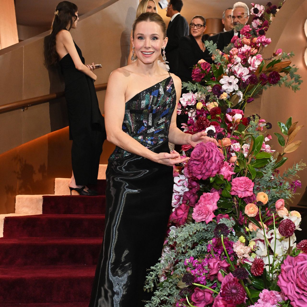Kristen Bell pointing to a gigantic pink rose on a staircase at the Golden Globes