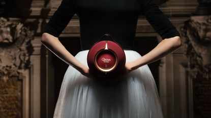 A women dressed as a ballet dancer holds the Devialet Mania Palais Garnier 150 Years Limited Edition in what appears to be an opera house. The photo is cropped so we see the woman's arms, top and skirt but not her head.
