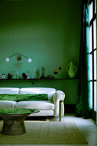 Modern living room with bright green walls, a white couch with a marbled green pillow on it, and a round coffee table. There is a shelf on the wall behind the couch that has various items along it including a lime green flower vase