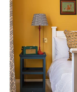 colorful bedroom with mustard yellow walls and blue bedside table