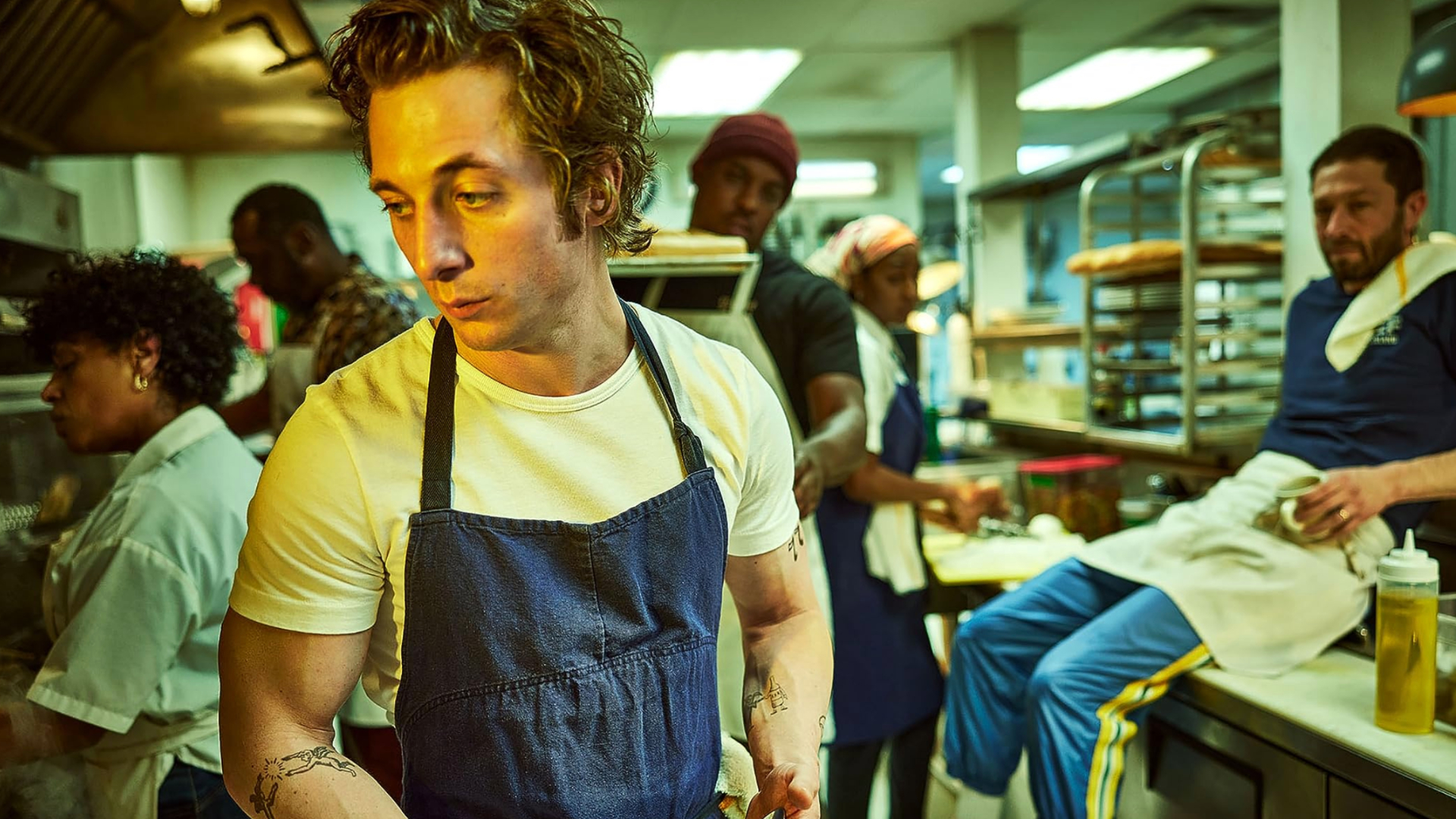 A screenshot of Carmy working in a kitchen as other people look on in The Bear