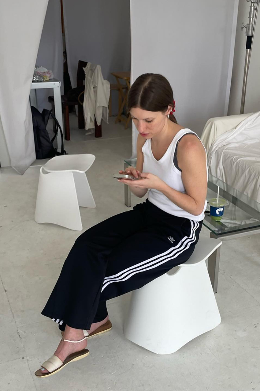 a woman wearing a pair of tack pants and a white tank top, and flat slides