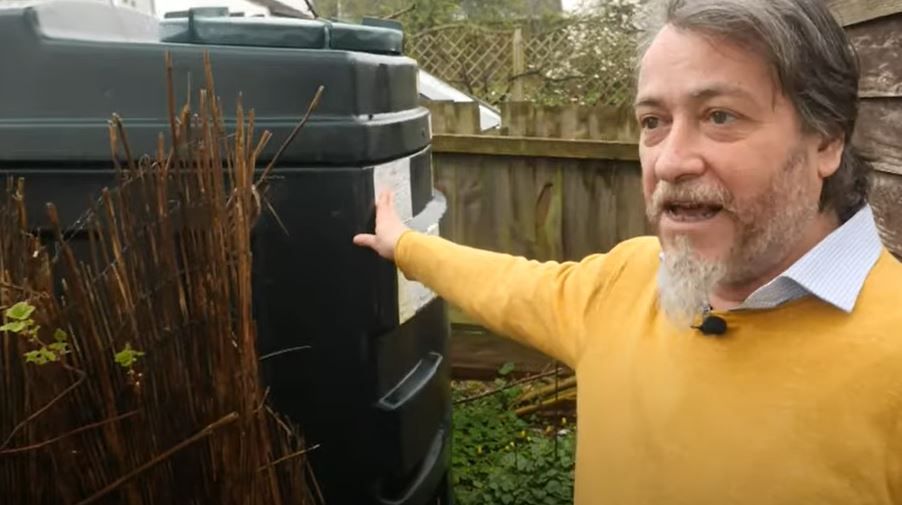 Mike Barker in a yellow jumper beside his old oil tank