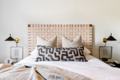 neutral bedroom with textural headboard, patterned throw cushions and two black wall lights