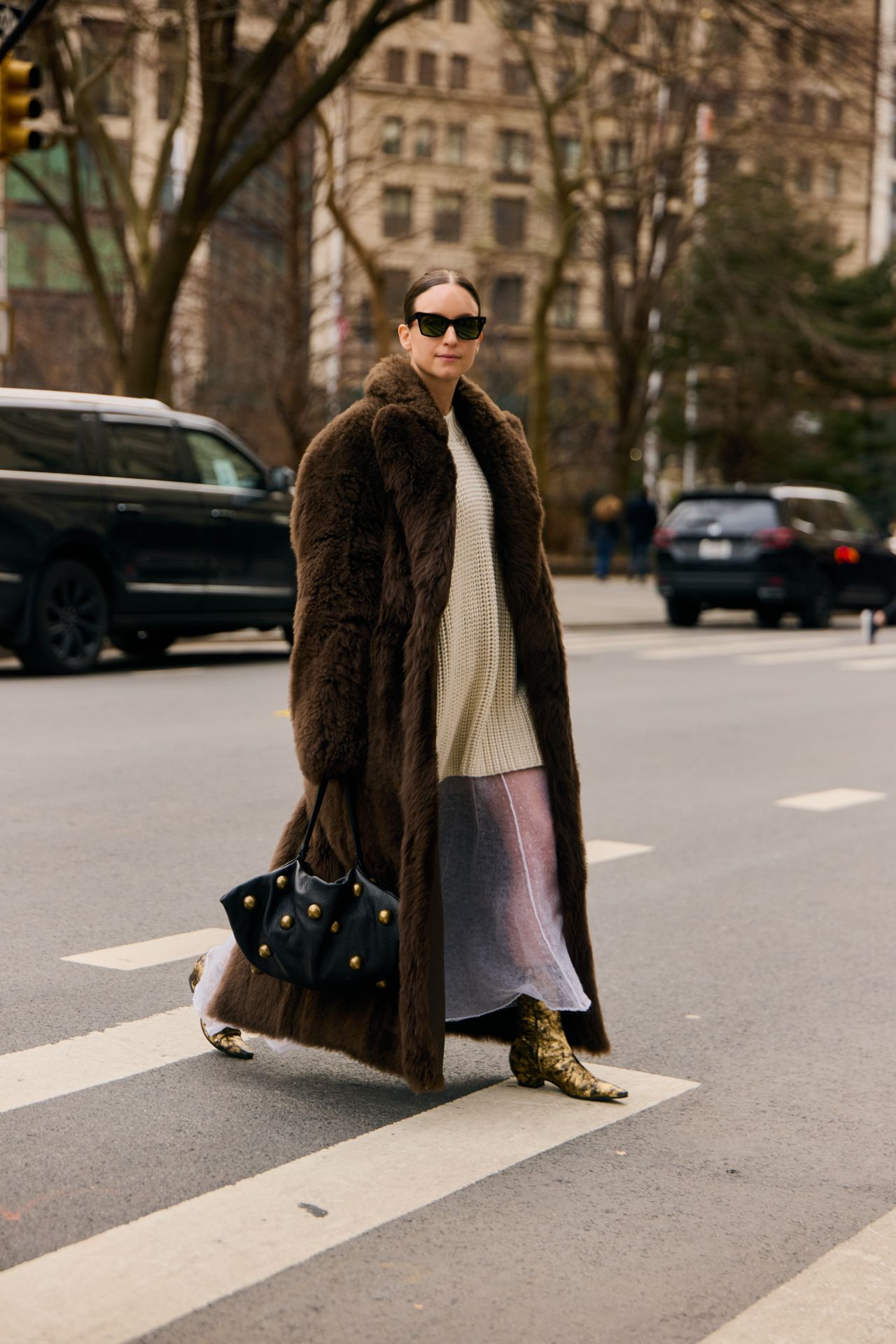A woman wearing a brown long fur coat, mini dress, and sheer skirt during F/W 25 fashion week in New York.