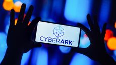 CyberArk logo and branding pictured on a smartphone screen held up in front of a blue blurry background.