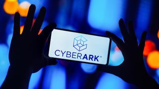 CyberArk logo and branding pictured on a smartphone screen held up in front of a blue blurry background.