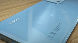 A light-blue Xiaomi 13 Lite camera phone sitting on a wooden desk