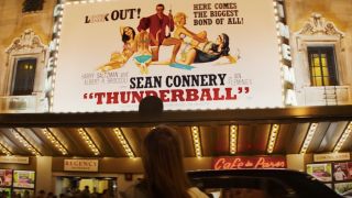Thomasin McKenzie looking up at a gigantic Thunderball poster in Last Night In Soho.
