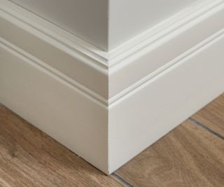 baseboard corner. Light matte wall with tiles immitating hardwood flooring