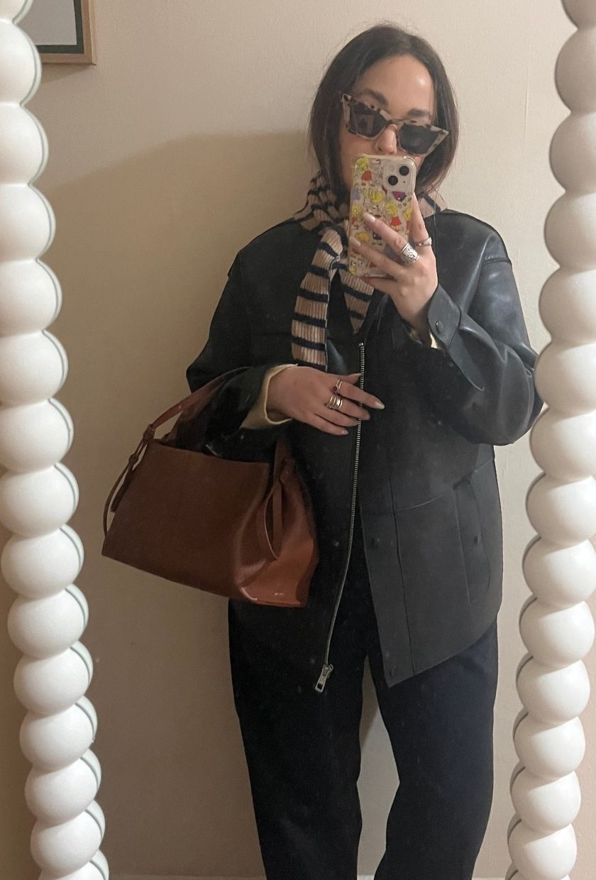 Woman wears leather jacket, tailored trousers and striped scarf