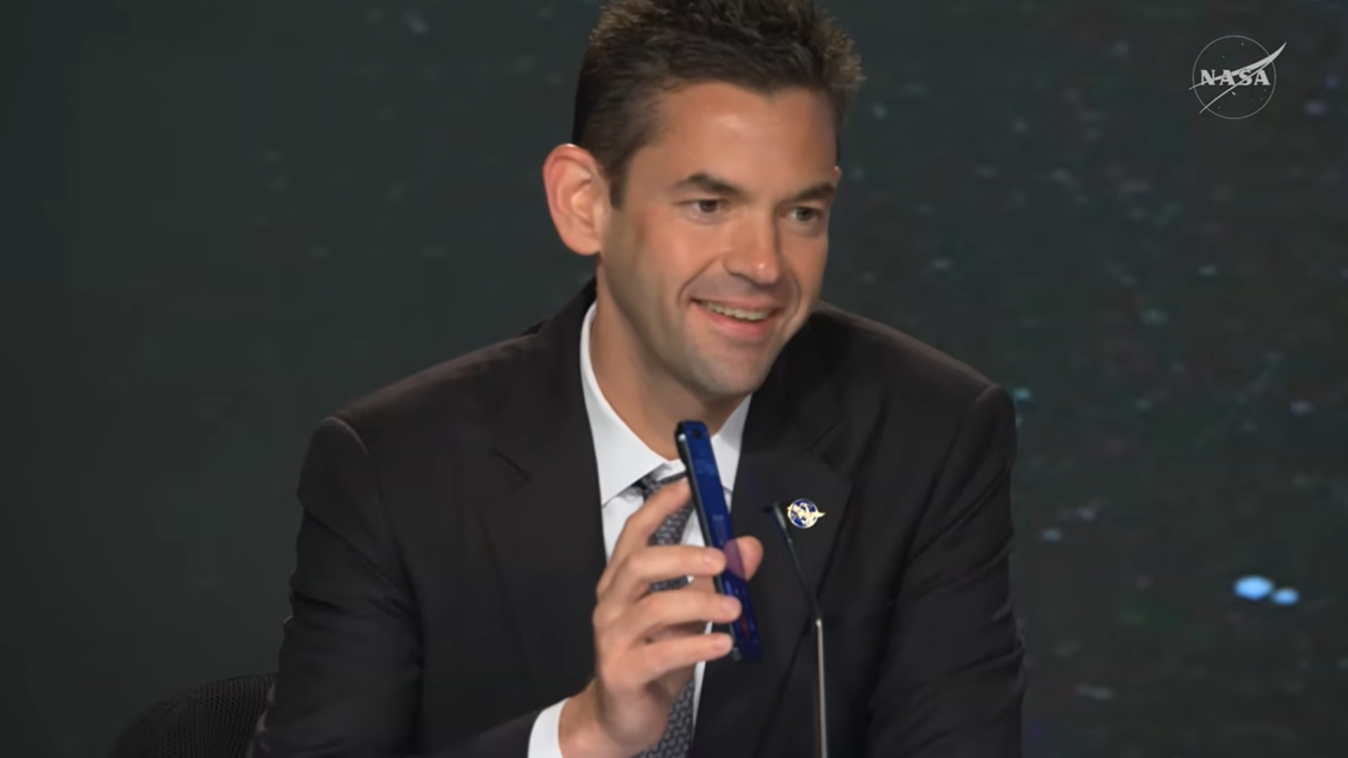 Jared Isaacman sostiene un teléfono celular cerca de un micrófono.