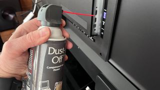 Hand holding compressed air can and using it to clean TV inputs