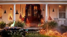 white shiplapped porch decorated for halloween by Terrain with hanging wicker witches hats, a door garland, lit brooms and pumpkins and a firepit