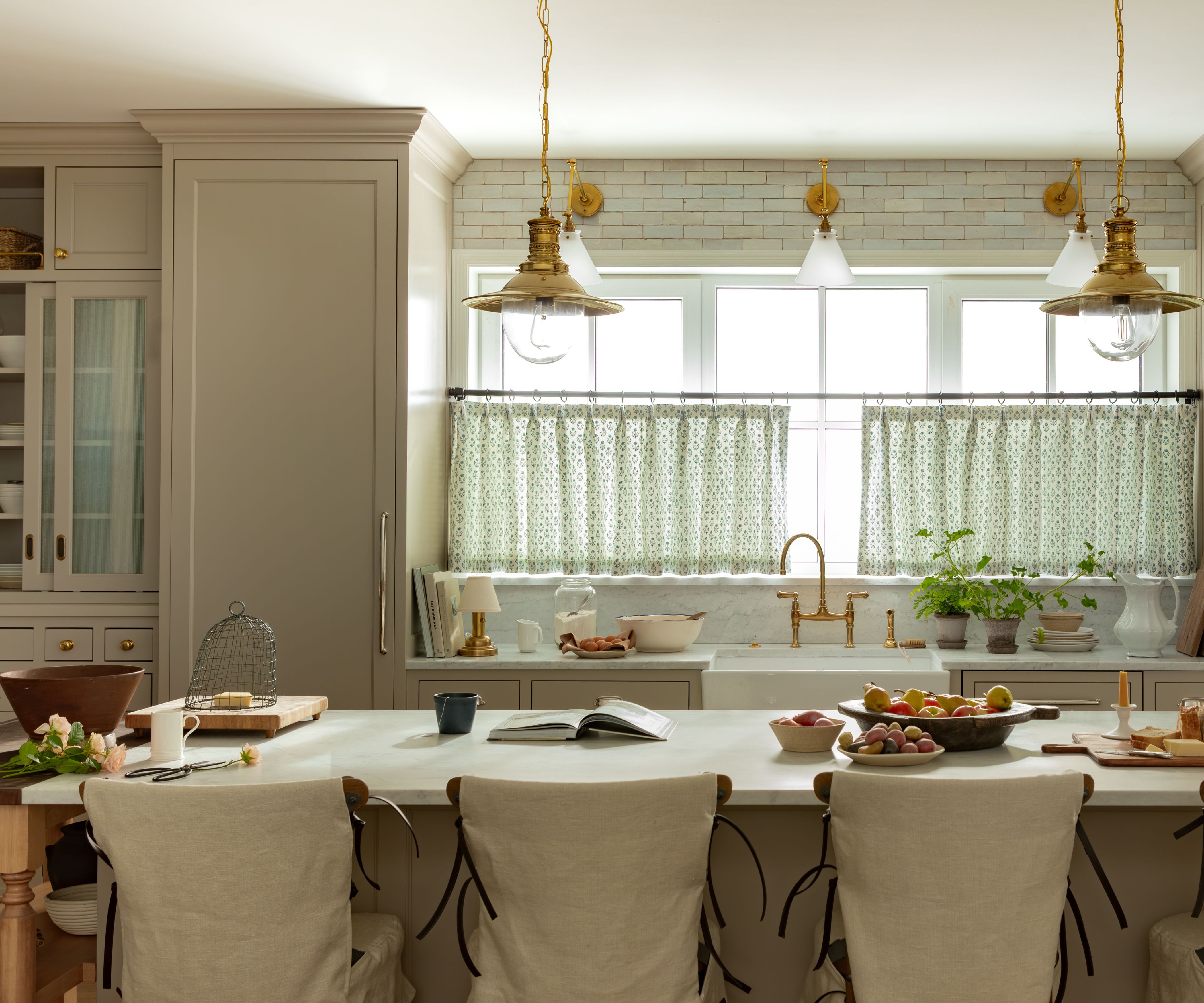 neutral warm beige farmhouse kitchen with vintage brass pendant lights over a large island with marble countertop and linen bar seating