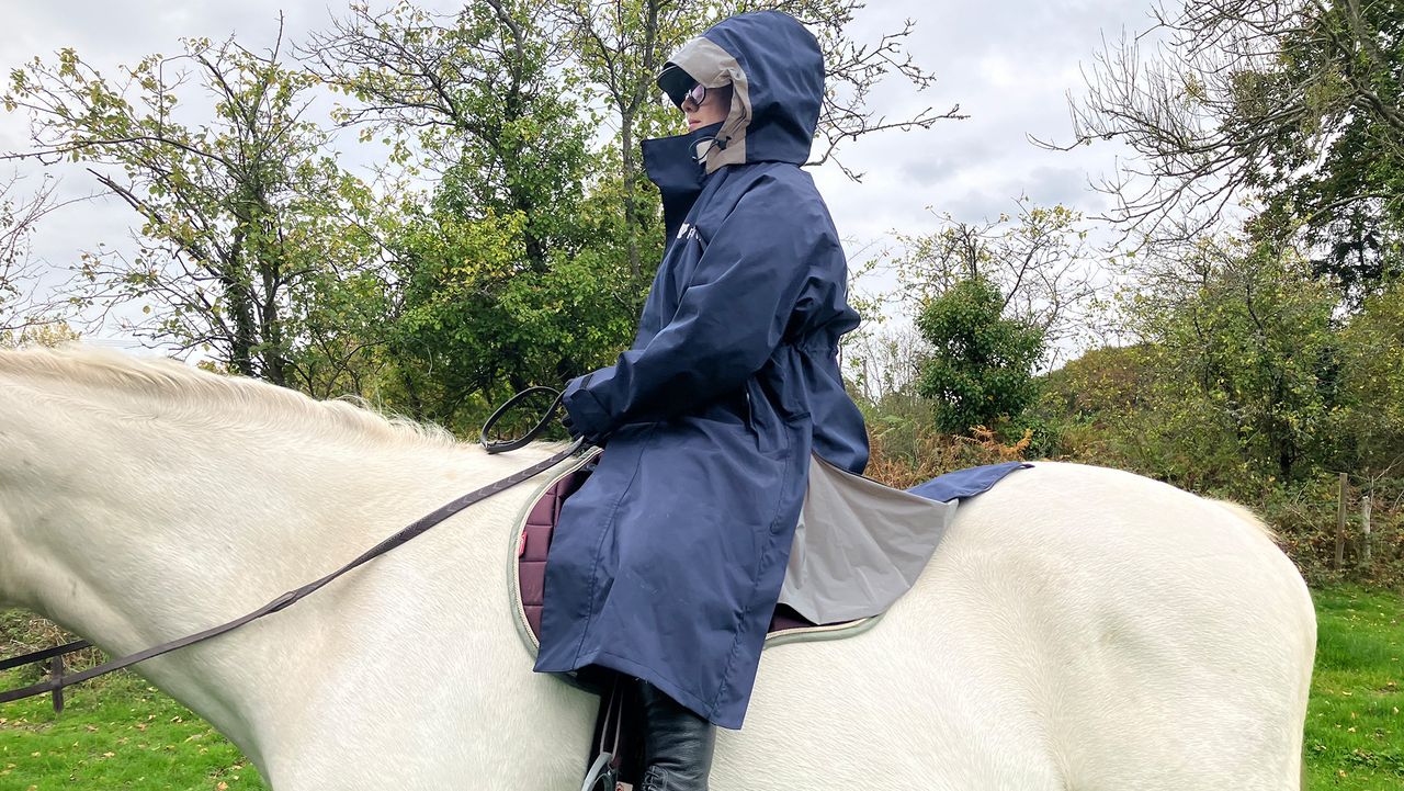 Rider wears Reincoat Lite on horse with hood up, viewed from the side
