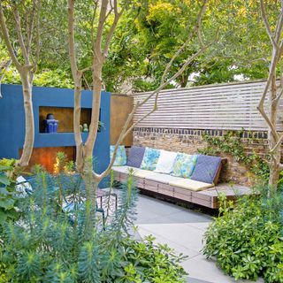 garden with blue painted wall and fireplace bench seating with cushions