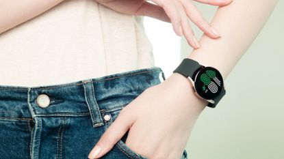 Samsung Galaxy Watch being worn by a woman with white skin, a cream top and blue jeans