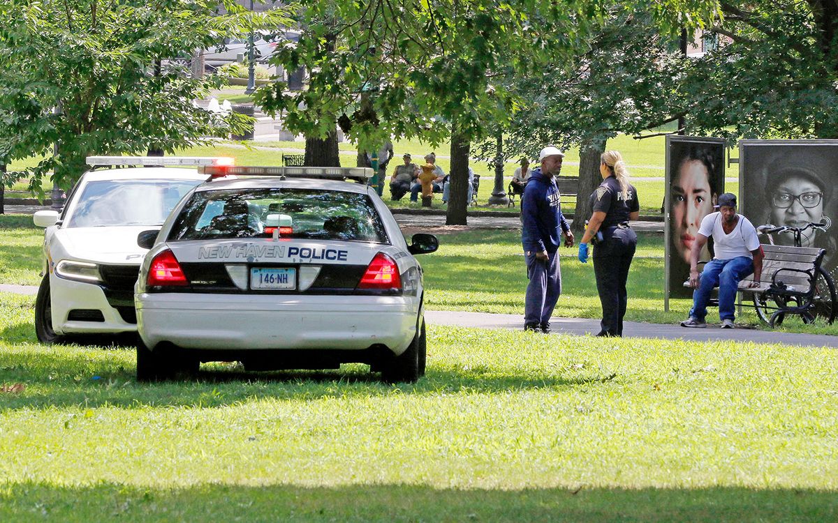  Several dozen people fell ill from suspected drug overdoses at New Haven Green park on Aug. 15. Above, a police officer speaks to a man walking on the Green.