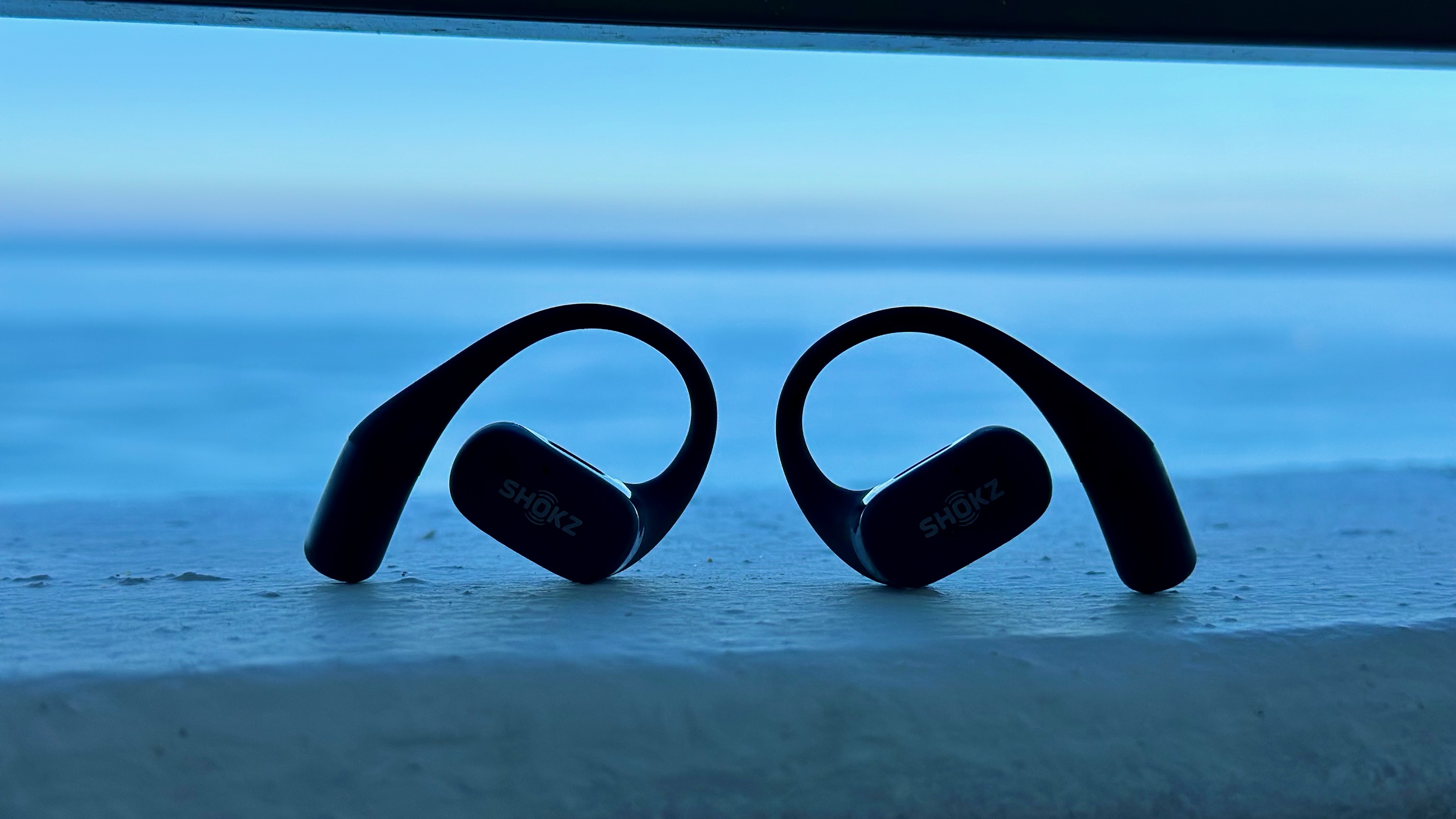 The Shokz OpenFit sitting upright in front of the ocean