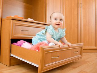 A baby sits in an open dresser drawer