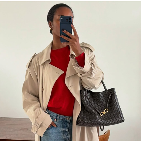 Woman wearing red t-shirt, trench coat, jeans, and brown Bottega Veneta Andiamo bag.