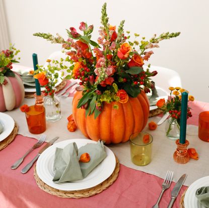 A Halloween themed tablescape with green candles and autumnal flowers in a pumpkin planter