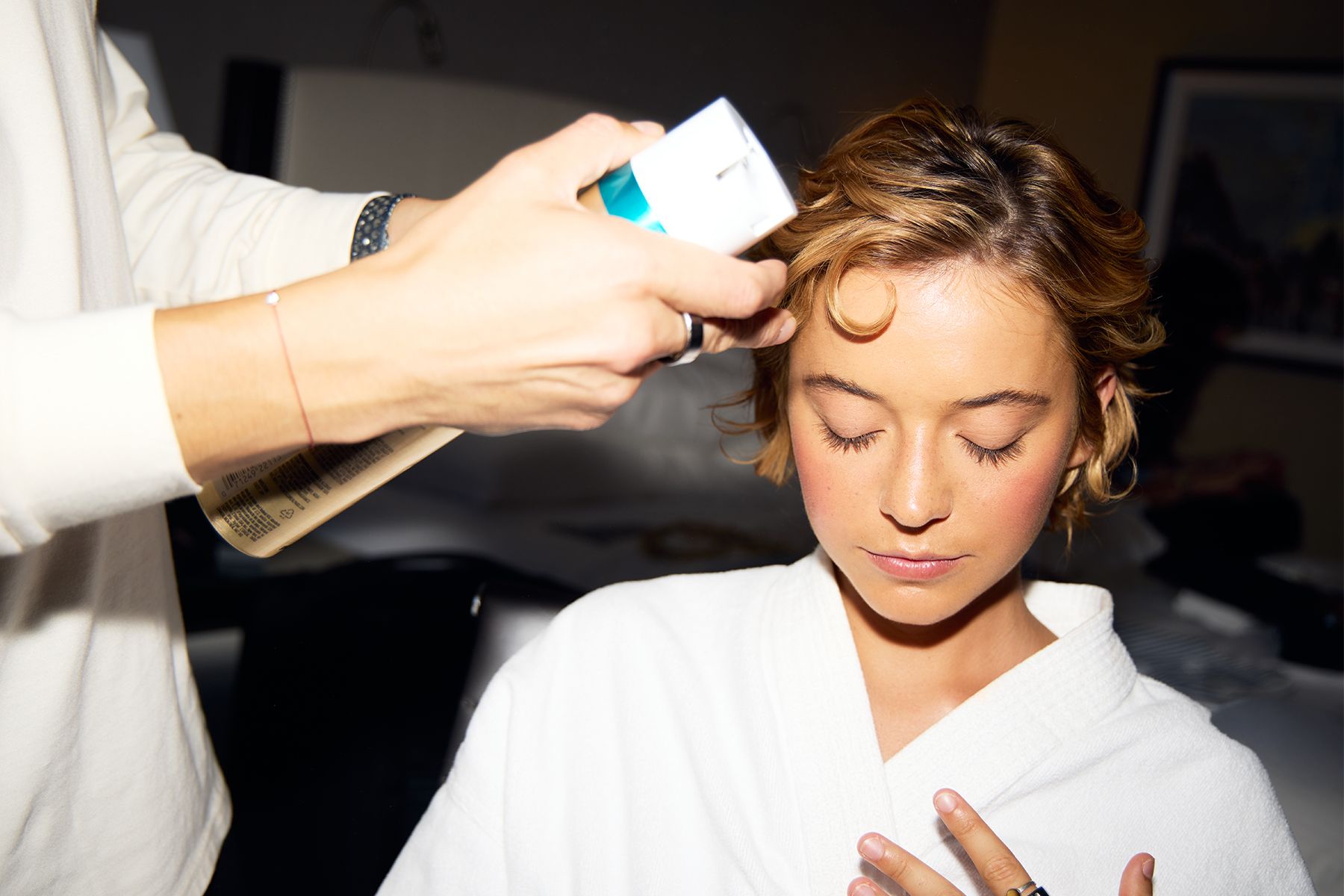 Sophie Telegadis is sitting in the glam chair wearing a white robe while her hairstylist Eduardo Bravo puts final touches on her TIFF look.