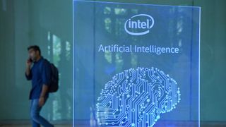 A man walks behind a glass sign displaying the Intel logo and the words 'artificial intelligence' above an image of a human brain