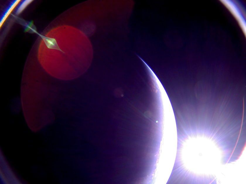 The Planetary Society’s LightSail 2 captured this picture of Earth’s limb on July 6, 2019, at 12:41 a.m. EDT from a camera mounted on its dual-sided solar panels. The spacecraft was headed into orbital sunset at the time, and the sun is visible to the right. The photo is unmodified and shows a number of lens flare artifacts caused by sunlight scattering around the camera optics. LightSail 2’s dual fisheye cameras have fields of view of about 180 degrees, causing the arcs in the corners and some distortion.