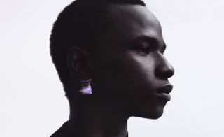 Man pictured to the side, wearing a purple crystal earring.