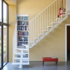 A large hallway with high ceilings and a curved staircase with the walls painted in Farrow & Ball's Hay shade