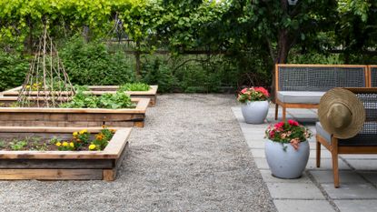 Backyard ideas on a budget, with raised vegetable beds, a gravel walkway and square paved patio area with bench seating.