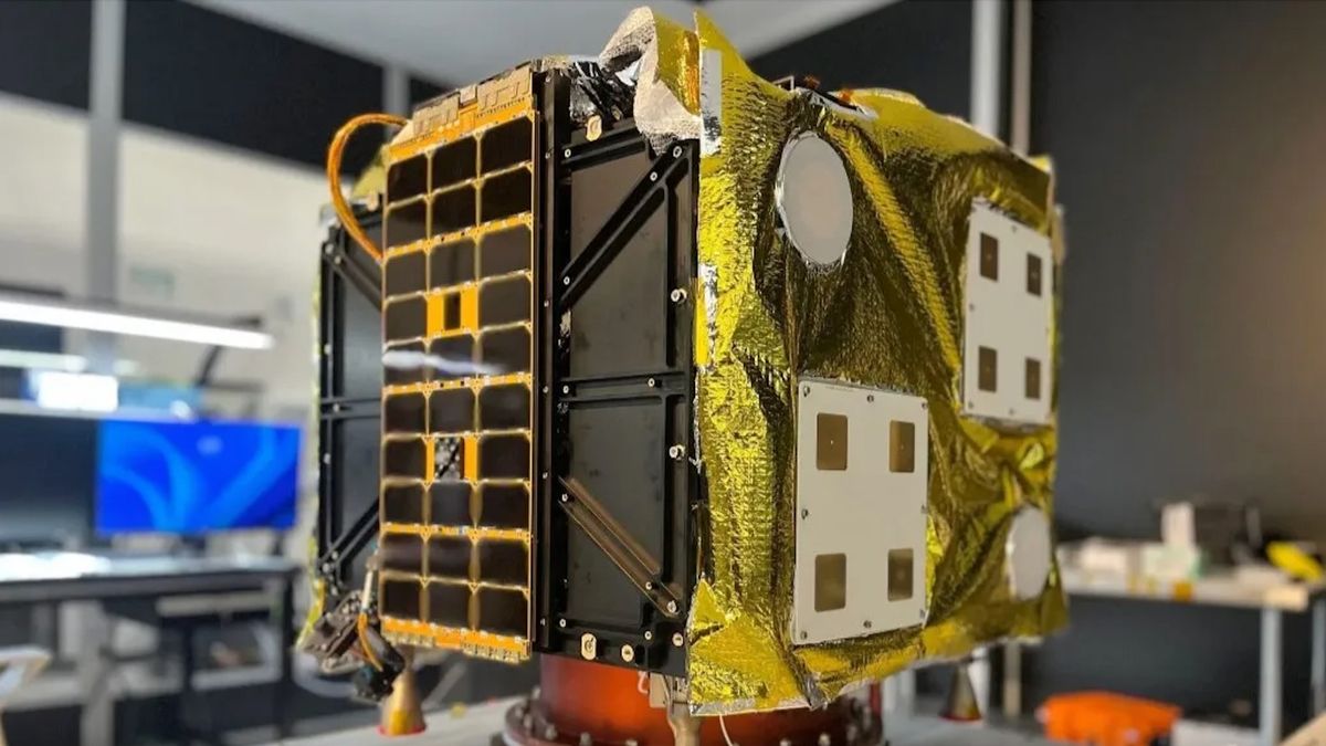 closeup of a small, boxy golden satellite inside a large room